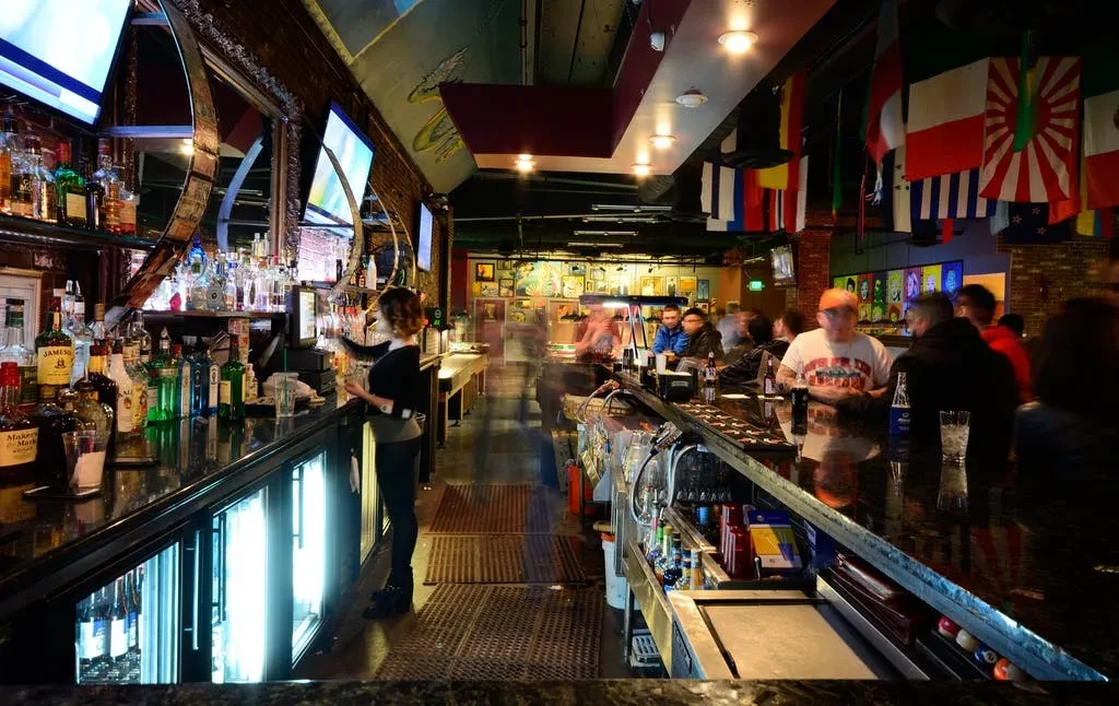 Lively bar interior with a well-stocked counter, bartender, and patrons.