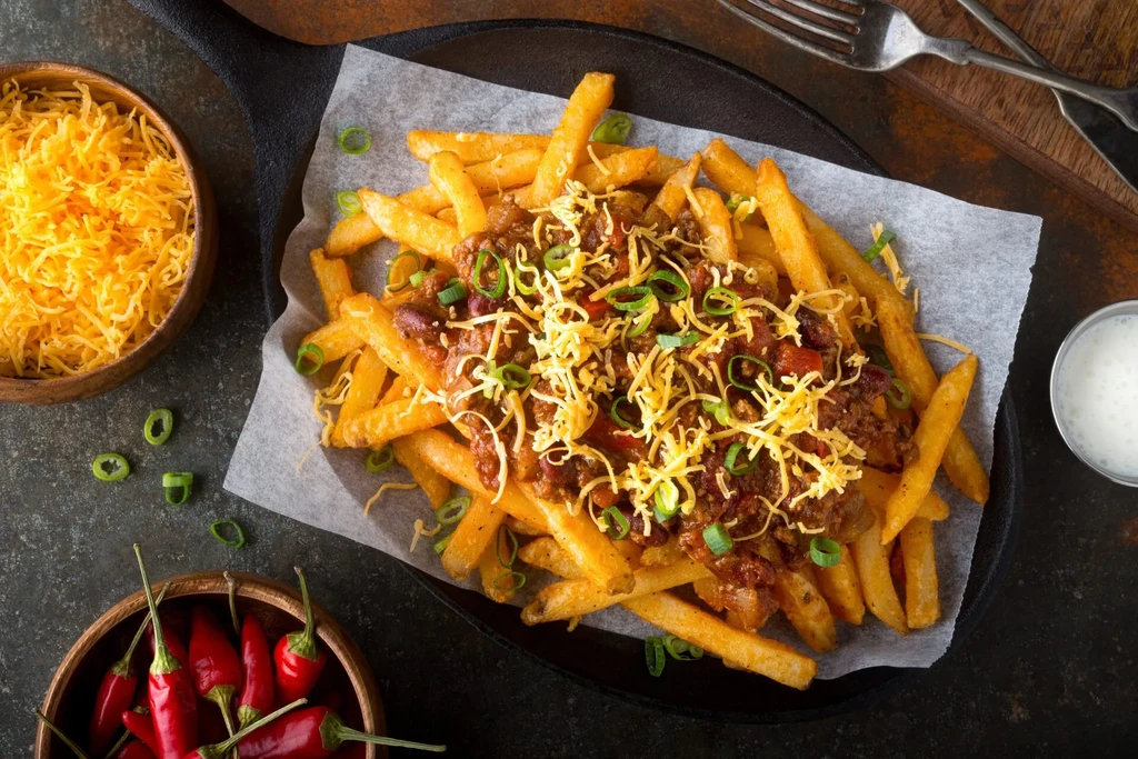 Overhead: Skillet of chili cheese fries, shredded cheese, peppers, and sour cream.