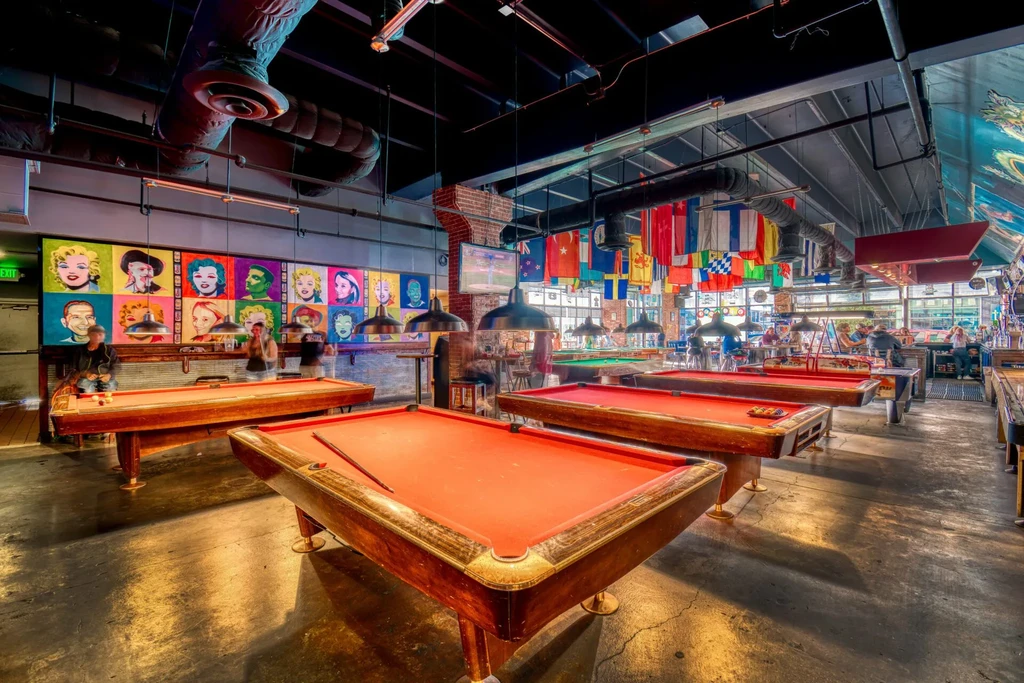 Lively entertainment venue interior with red pool tables and pop art mural.