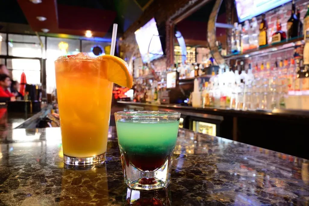 Orange drink with orange and layered shot on a bar.