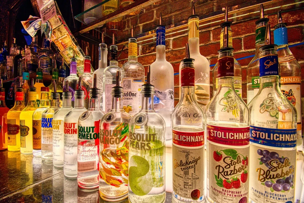 Many vodka and spirit bottles line a reflective bar counter.