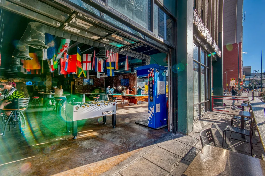 Open-front bar with foosball, pool, international flags, and street view.