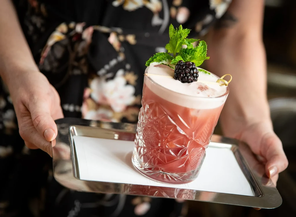 Red foamy cocktail with blackberry and mint on a silver tray.