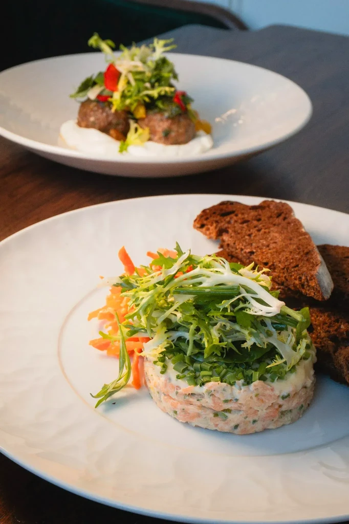 Close-up of salmon tartare with bread; savory patties in blurred background.