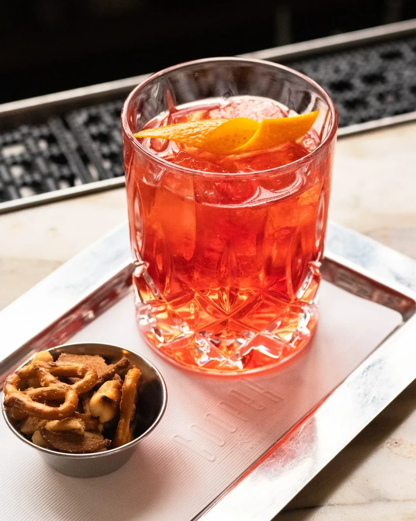 Red cocktail and pretzel snack on a silver tray.