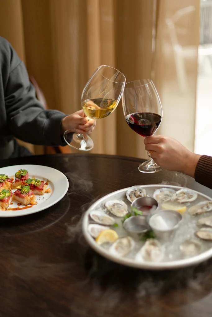 Hands toast with wine over tuna tartare and oysters on ice.