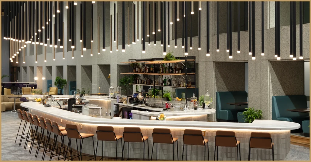 Empty modern bar with curved white counter, brown stools, and pendant lights.