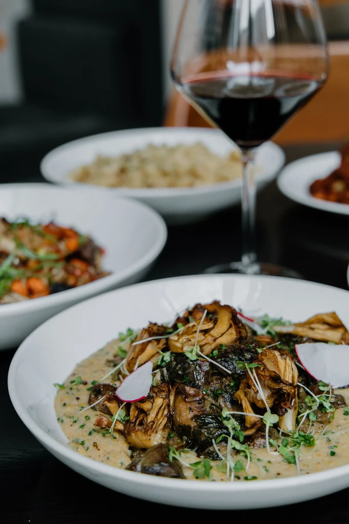 Creamy mushroom dish, two other dishes, and a focused red wine glass.
