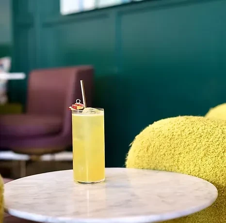 Yellow drink with ice, fruit slice, straw on marble table.