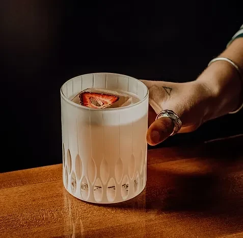 Ringed hand holds frosted glass cocktail with dried strawberry.
