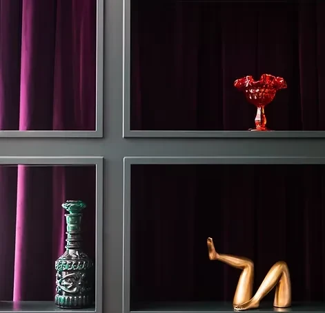 Multi-panel shelving displaying red goblet, green decanter, and golden leg sculpture.