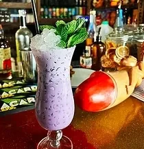 Vibrant purple cocktail with mint, ice, and straw on a bar.