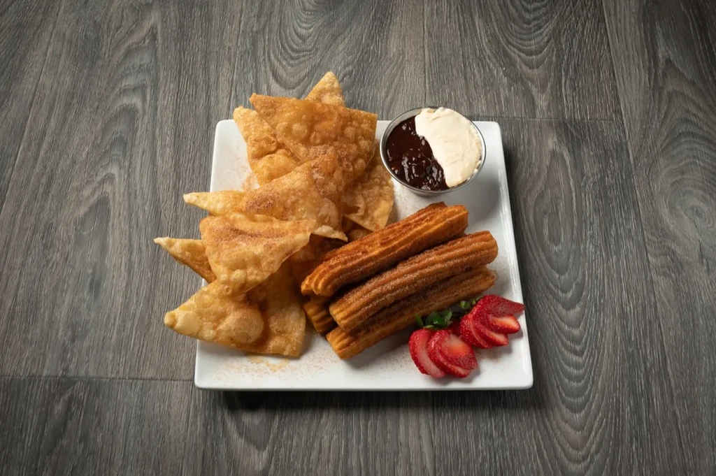 Plate of churros, fried wonton crisps, sauces, and sliced strawberries.