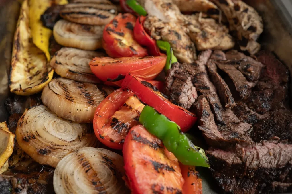 Overhead view of grilled zucchini, onions, peppers, tomatoes, chicken, and steak.