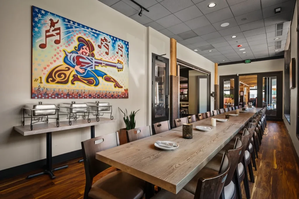 Spacious restaurant interior with a long dining table, buffet, and colorful art.