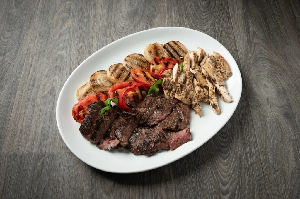 Grilled medium-rare steak, chicken, charred vegetables on a white platter.