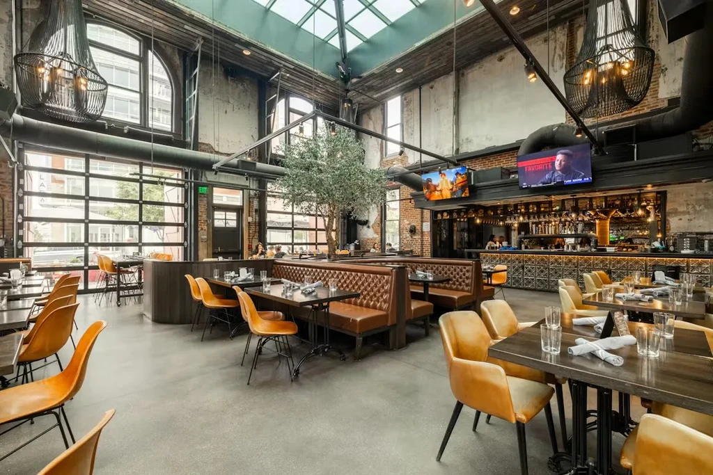 Industrial-chic restaurant interior with dining, bar, and high ceilings.