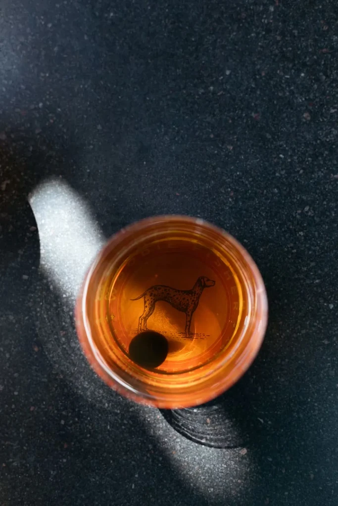 Overhead view: amber drink in glass with a Dalmatian illustration.