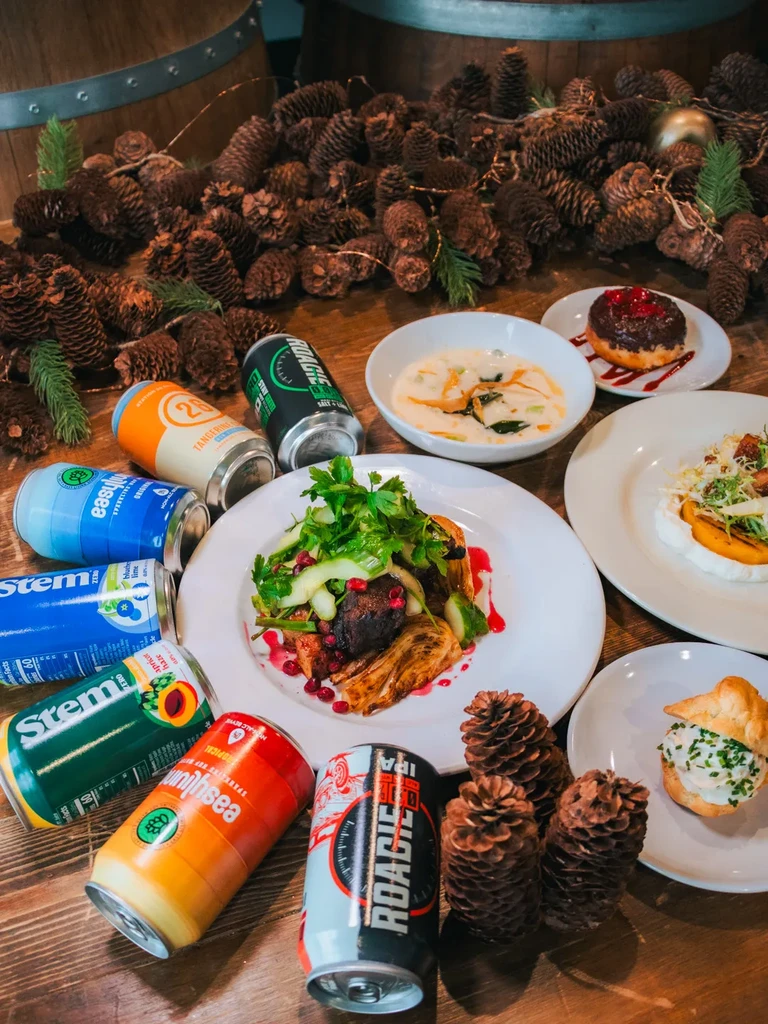 Overhead view: rustic table with food, drinks, pinecones, and string lights.