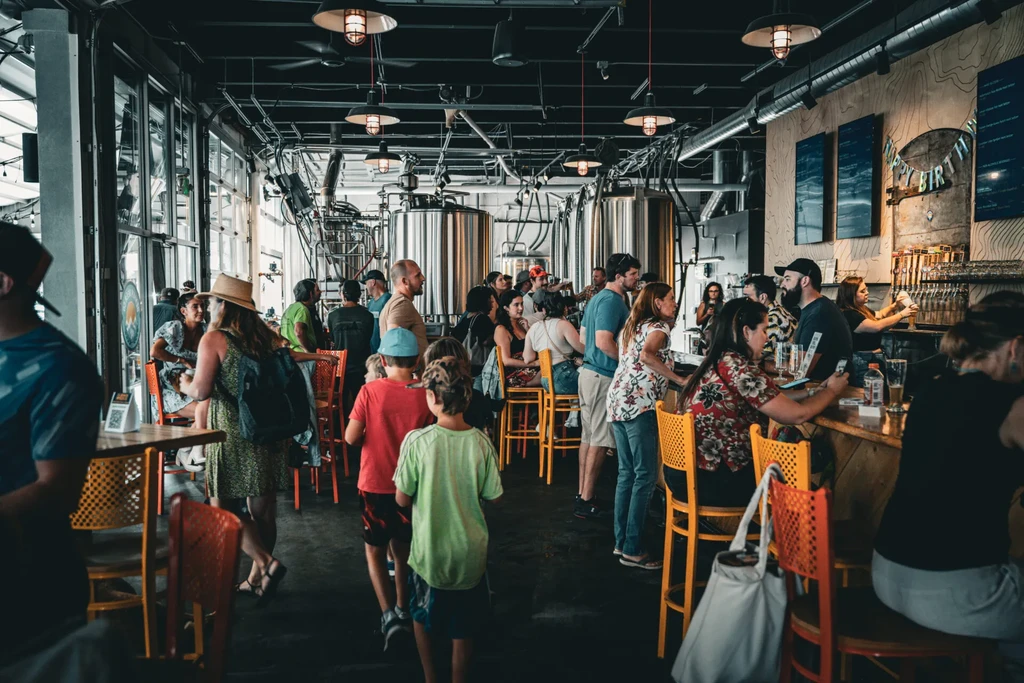 Crowded modern brewery with brewing tanks and a "Happy Birthday" banner.