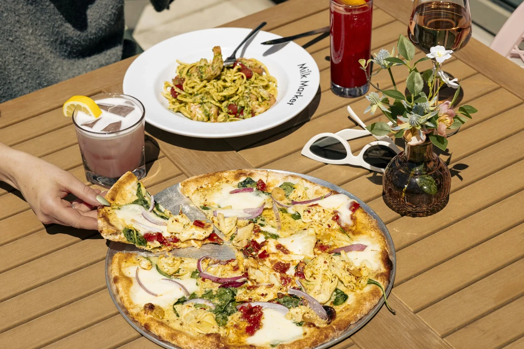 Hand reaching for a slice of pizza, pesto pasta, and drinks.