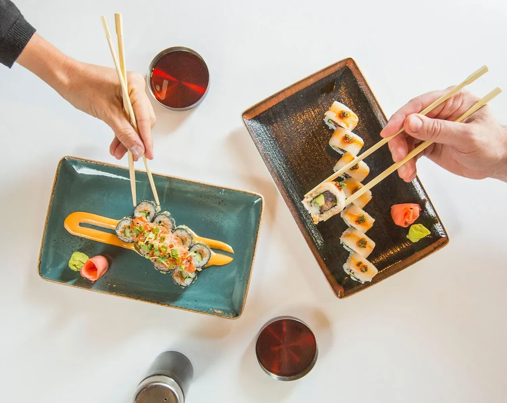Overhead shot of two hands using chopsticks to eat sushi rolls.
