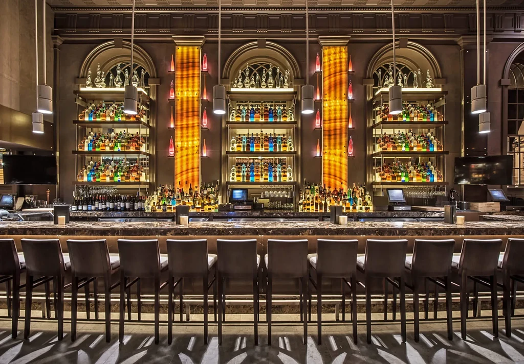 Luxurious bar with long counter, many stools, and elaborate backlit liquor display.
