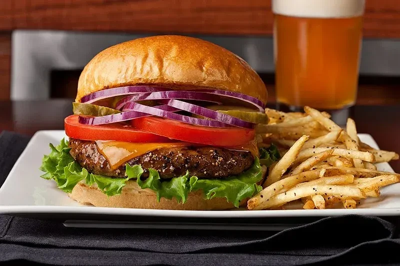Close-up cheeseburger, fries, and beer on a white plate.