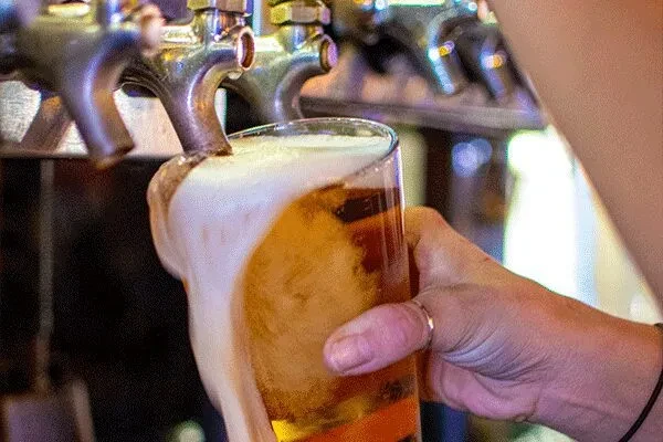 Golden beer overflows from a glass being poured from a tap.