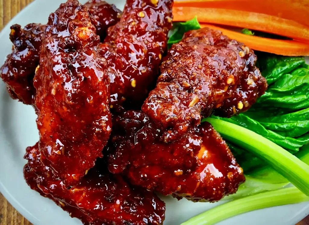 Glossy glazed chicken wings with green and orange vegetables.