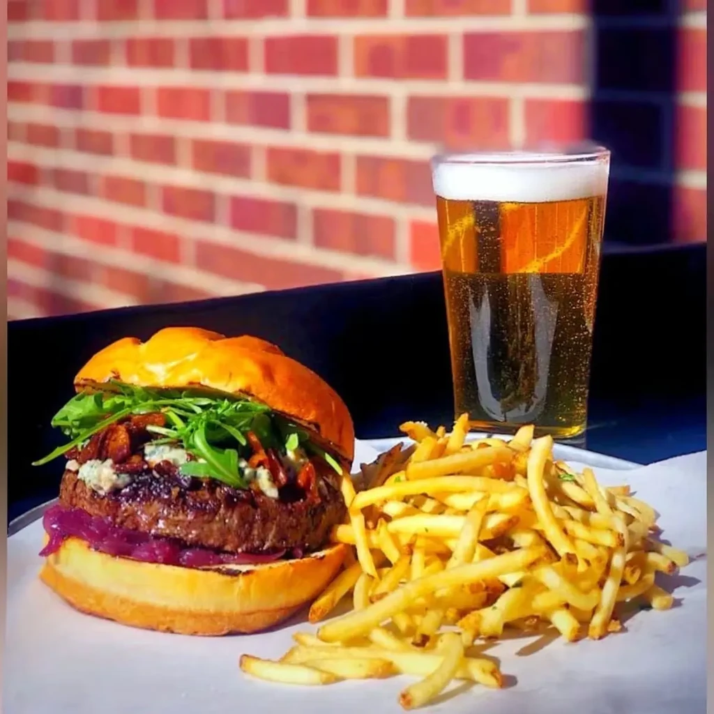 Close-up of gourmet burger, golden fries, and amber beer, brick wall.