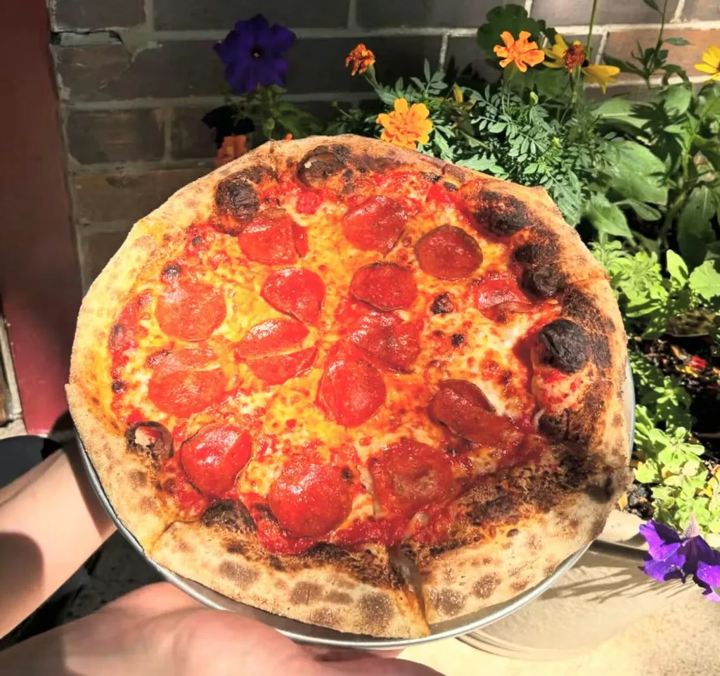Neapolitan pepperoni pizza with leopard-spotted crust, held outdoors.
