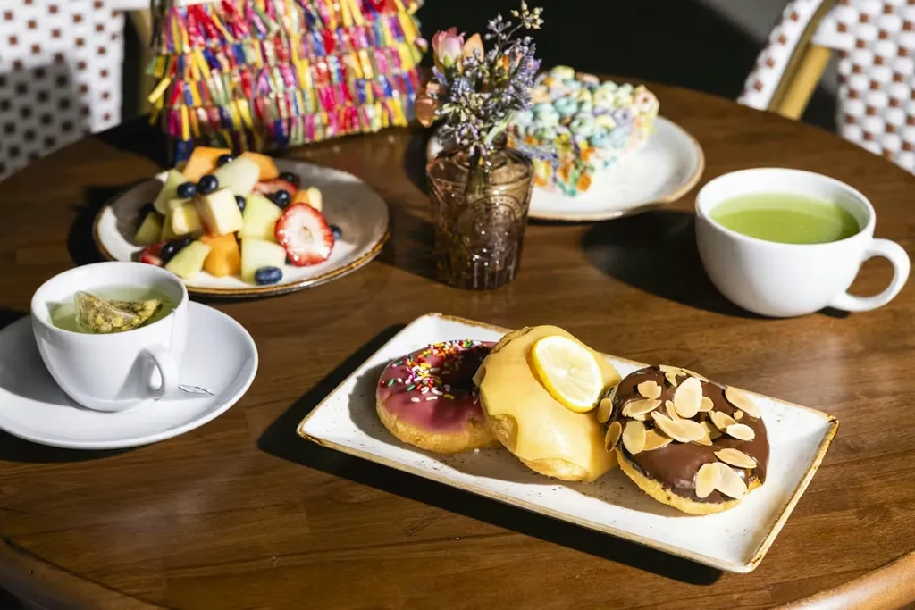 Donuts, fruit salad, herbal tea, and matcha on a wooden table.