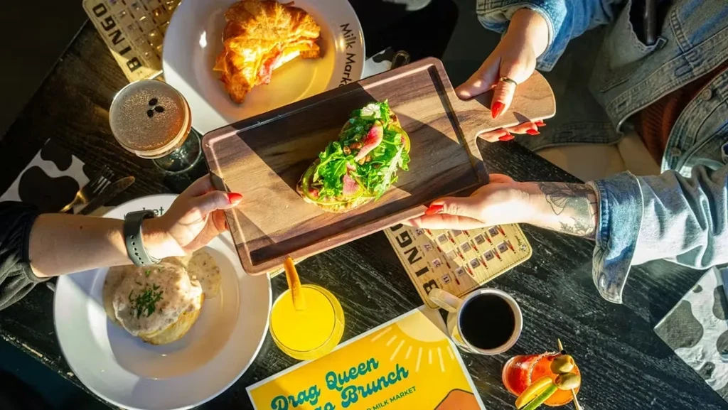 Vibrant overhead brunch table with croissant, biscuits, drinks, and four hands.