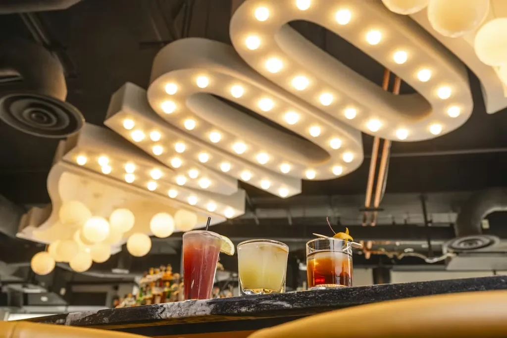 Three cocktails on a bar under a glowing marquee sign.