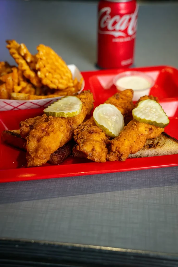 Fried chicken tenders with pickles, waffle fries, sauce, and Coke.