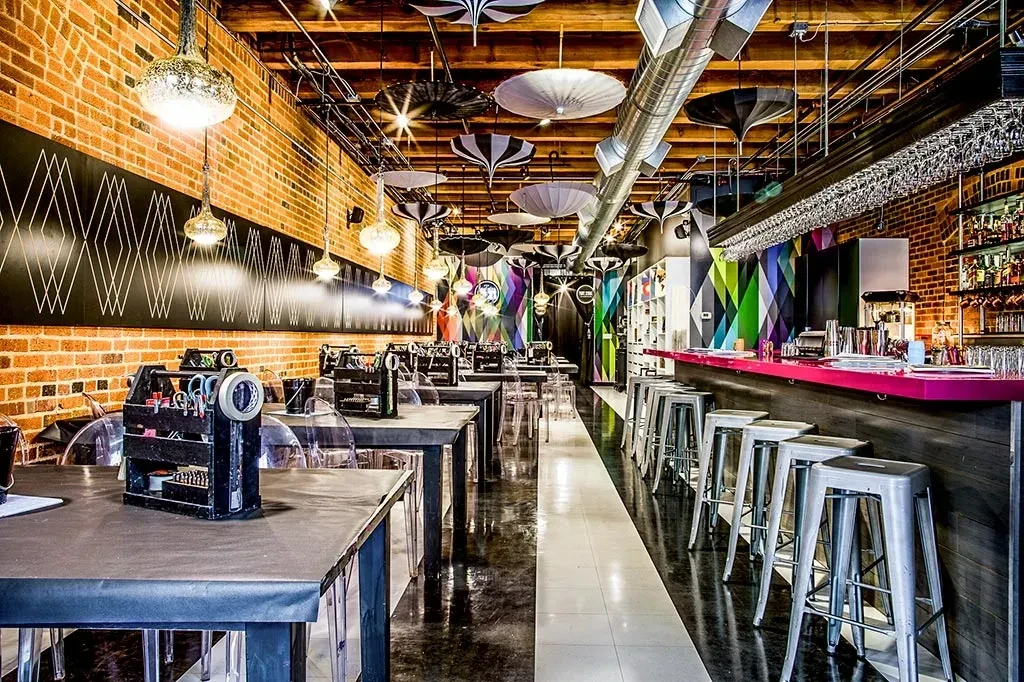 Industrial-eclectic interior with a pink bar, geometric walls, and exposed brick.