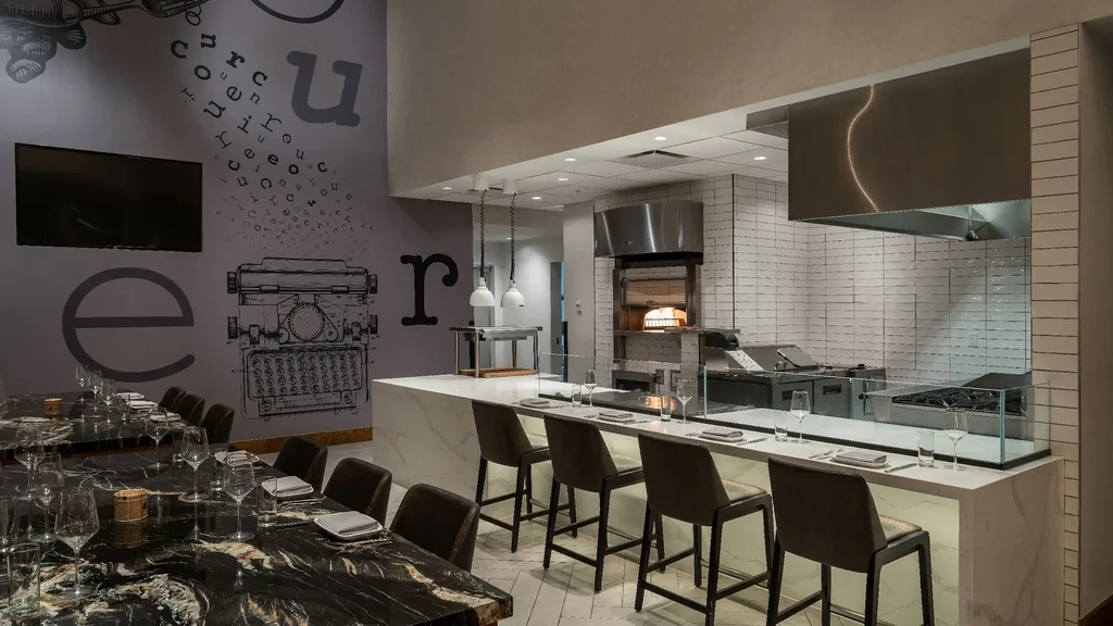Modern restaurant with marble dining, open kitchen, and typewriter wall art.
