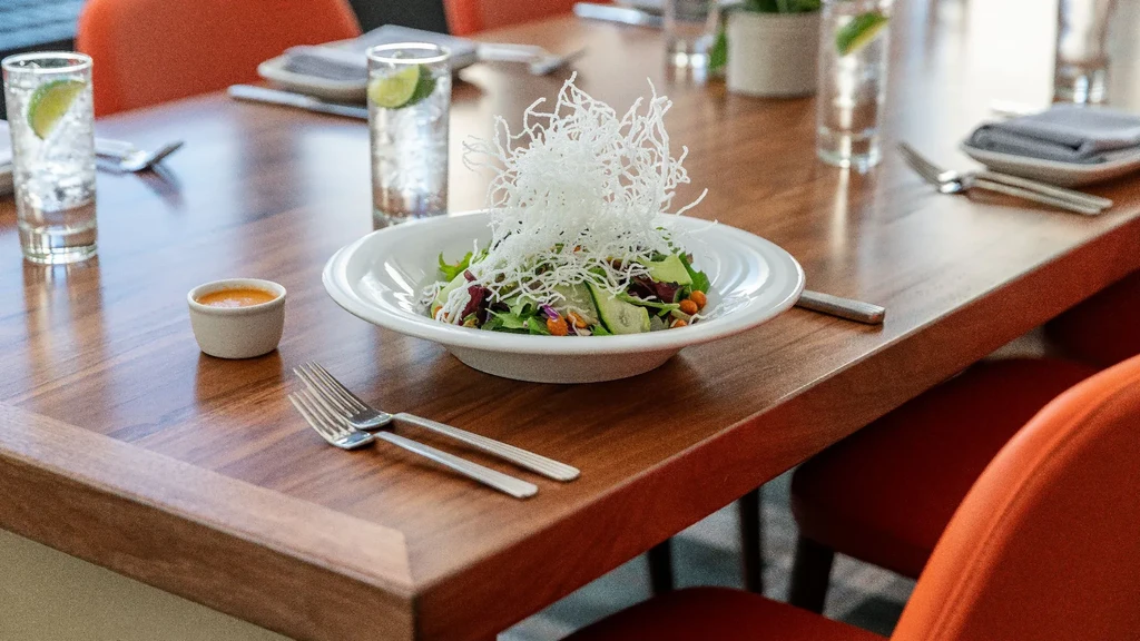 Vibrant salad with crispy garnish, orange dressing on a modern wooden table.
