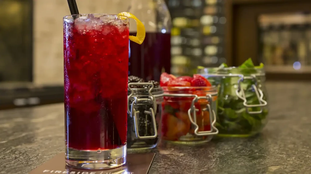 Red cocktail with ice, lemon twist, muddled fruit, and fresh ingredients.