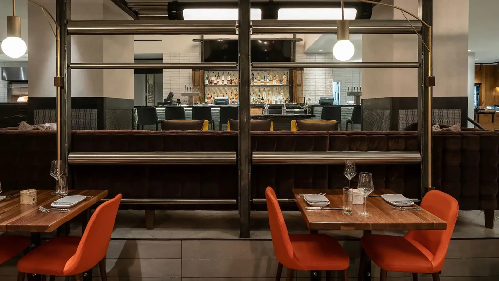 Modern restaurant interior with orange chairs, banquettes, and a well-stocked bar.