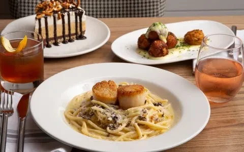 Restaurant table: pasta with scallops, cocktail, wine, appetizer, and cake.