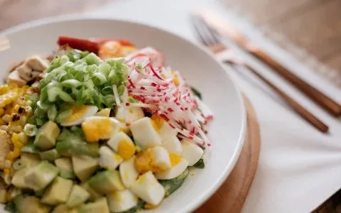 A vibrant salad bowl with avocado, eggs, grilled corn, and radishes.