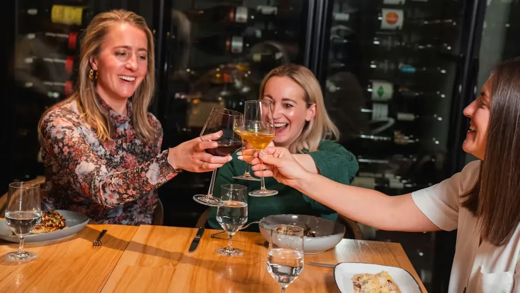 Three smiling women toast with wine glasses in a restaurant.