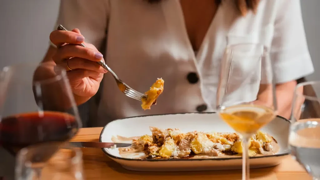 Hand with purple nail polish lifts pasta from plate; drinks visible.