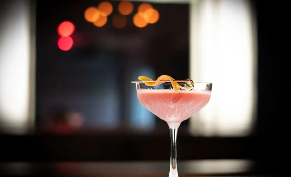 Creamy pink cocktail in ornate coupe with citrus peel.