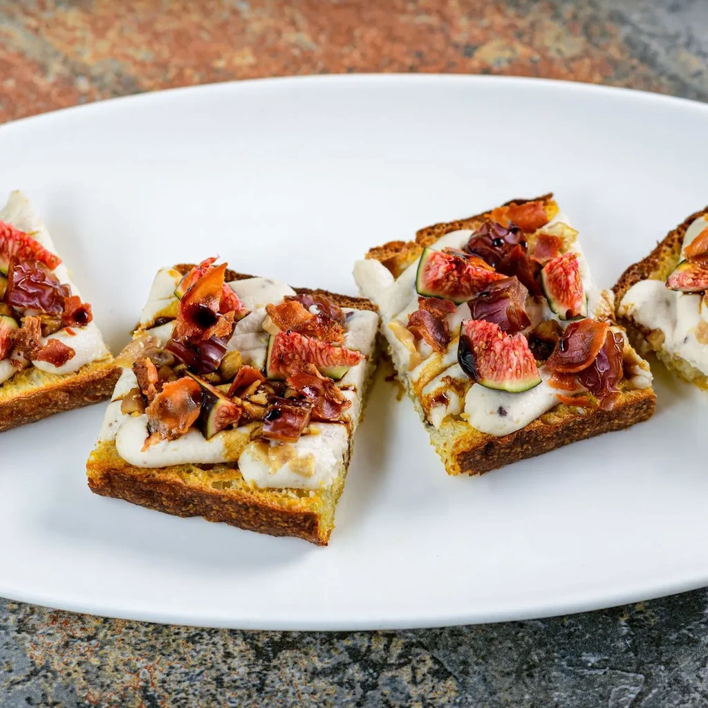 Four bruschetta topped with figs, caramelized onions, prosciutto, and balsamic glaze.