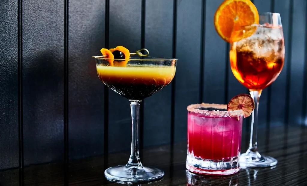 Three colorful cocktails in different glasses with diverse garnishes.