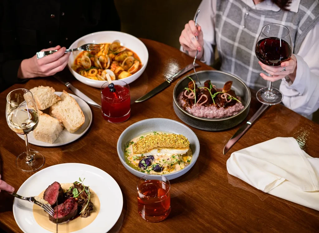 Overhead view of four gourmet dishes, drinks, and two people dining.