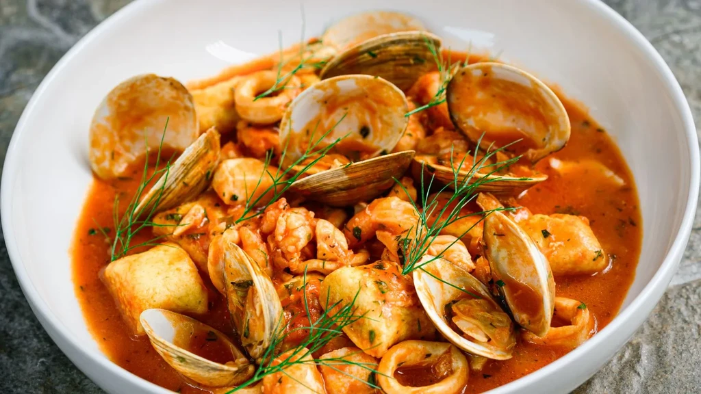 Close-up of vibrant seafood stew with clams, shrimp, and green herbs.